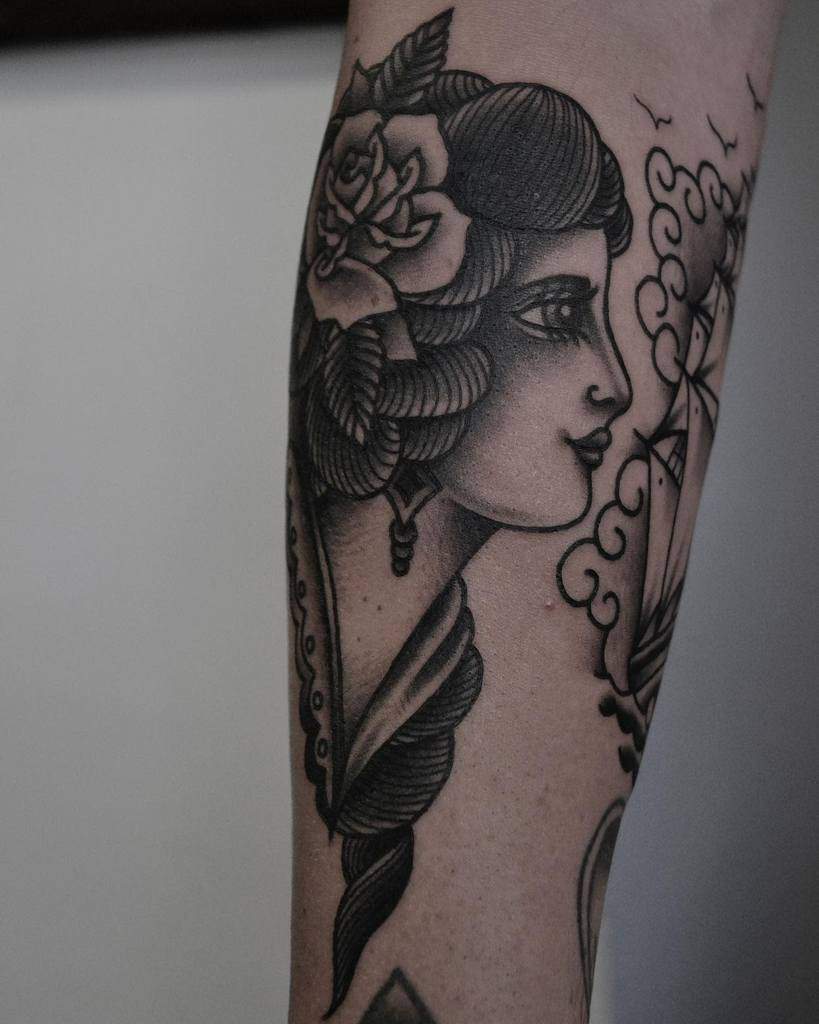 Tattoo of a gypsy woman's profile with a rose in her hair, alongside a sailing ship