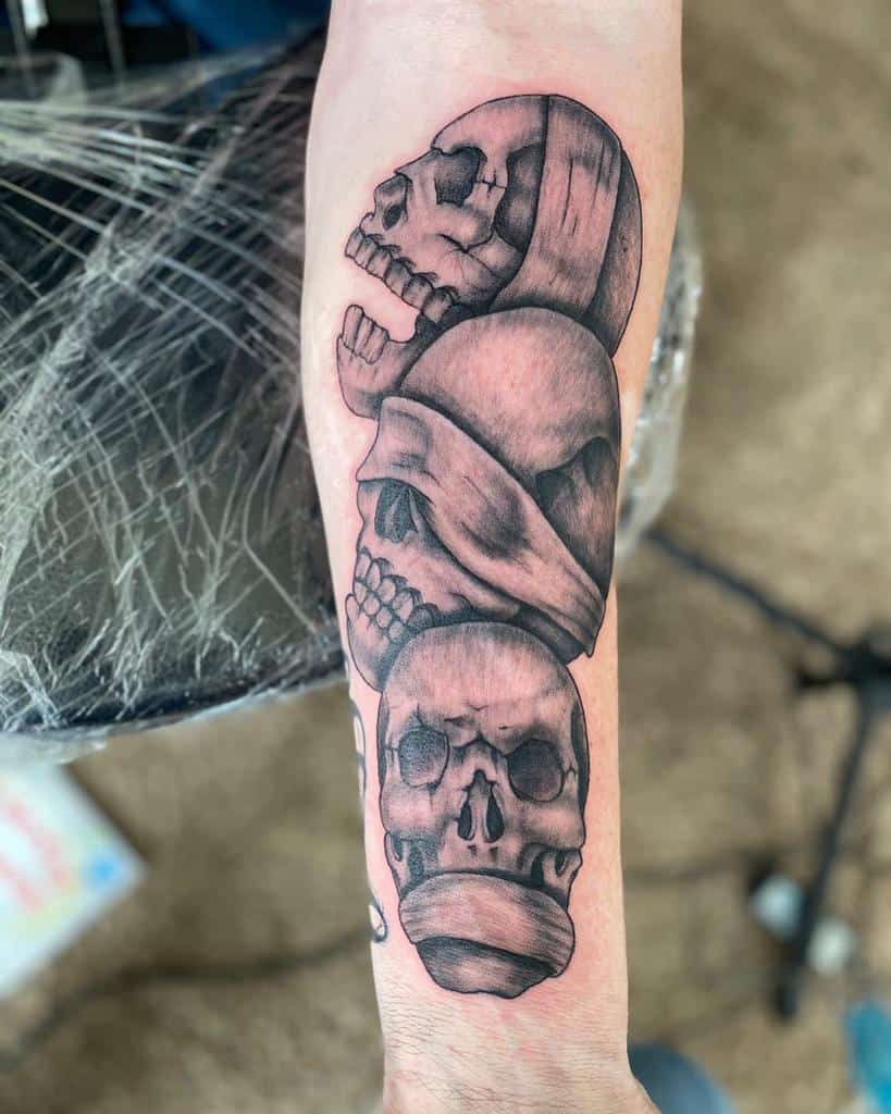 Forearm tattoo of three stacked skulls representing 'Hear No Evil, See No Evil, Speak No Evil,' with bold shading and texture