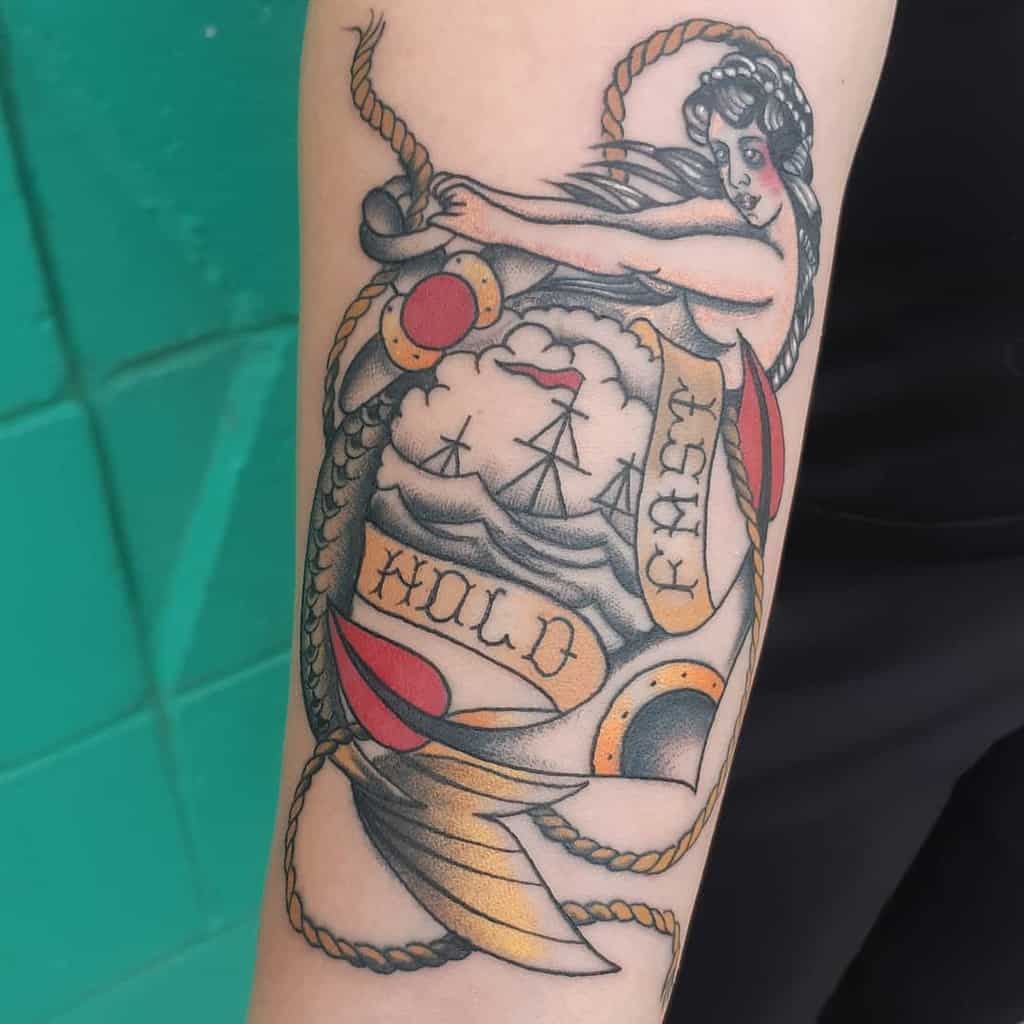 Tattoo of a woman, ship, and banners reading "HOLD FAST" on an arm