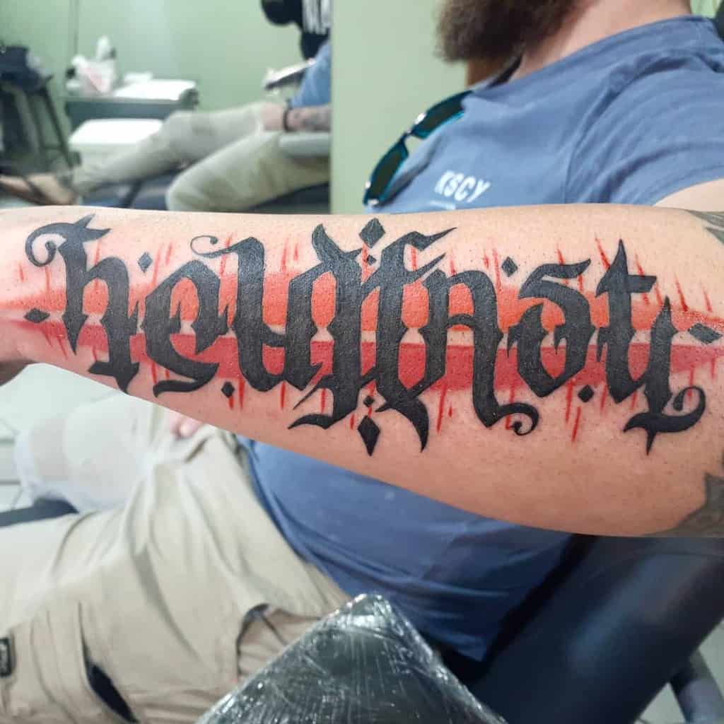 Tattooed arm with the word "holdfast" in bold, gothic style lettering