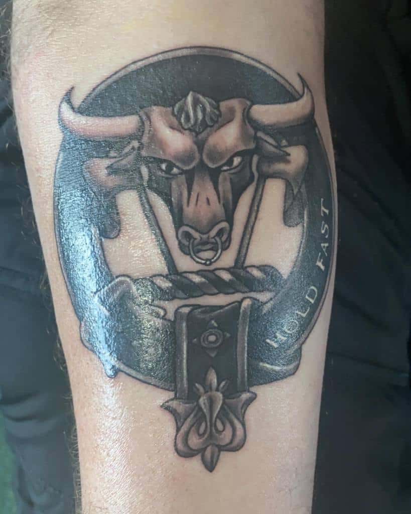 Tattoo of a bull's head inside a circle with the words "HOLD FAST" on an arm