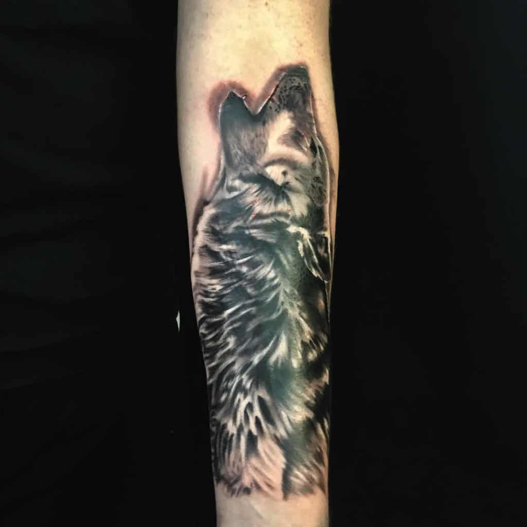 A stunningly realistic tattoo featuring a lone wolf howling graces the forearm, capturing the wild essence of nature