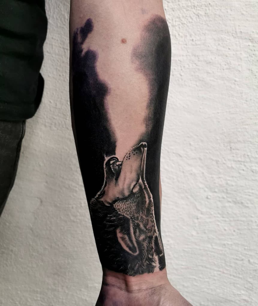 Forearm tattoo featuring a wolf howling against a dark, smoky backdrop