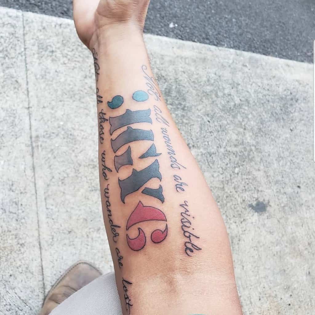 Forearm tattoo featuring ';IGY6' with a blue semicolon, red 6, and the phrases 'Not all wounds are visible' and 'Not all who wander are lost'