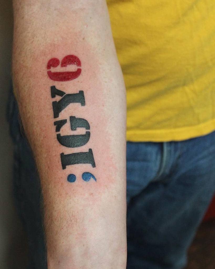 Forearm tattoo featuring 'IGY6' in bold lettering, with a blue semicolon and a red number 6 symbolizing support