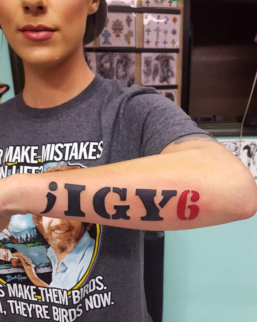 Woman showing an arm tattoo with the text ";IGY6" in black and red