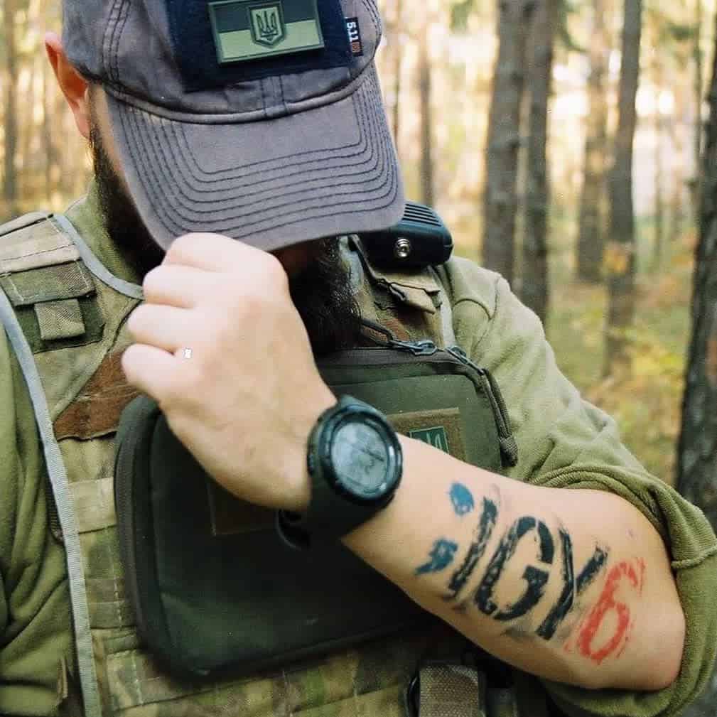 A man with a tattoo on his forearm that reads ";IGY6" with colored accents