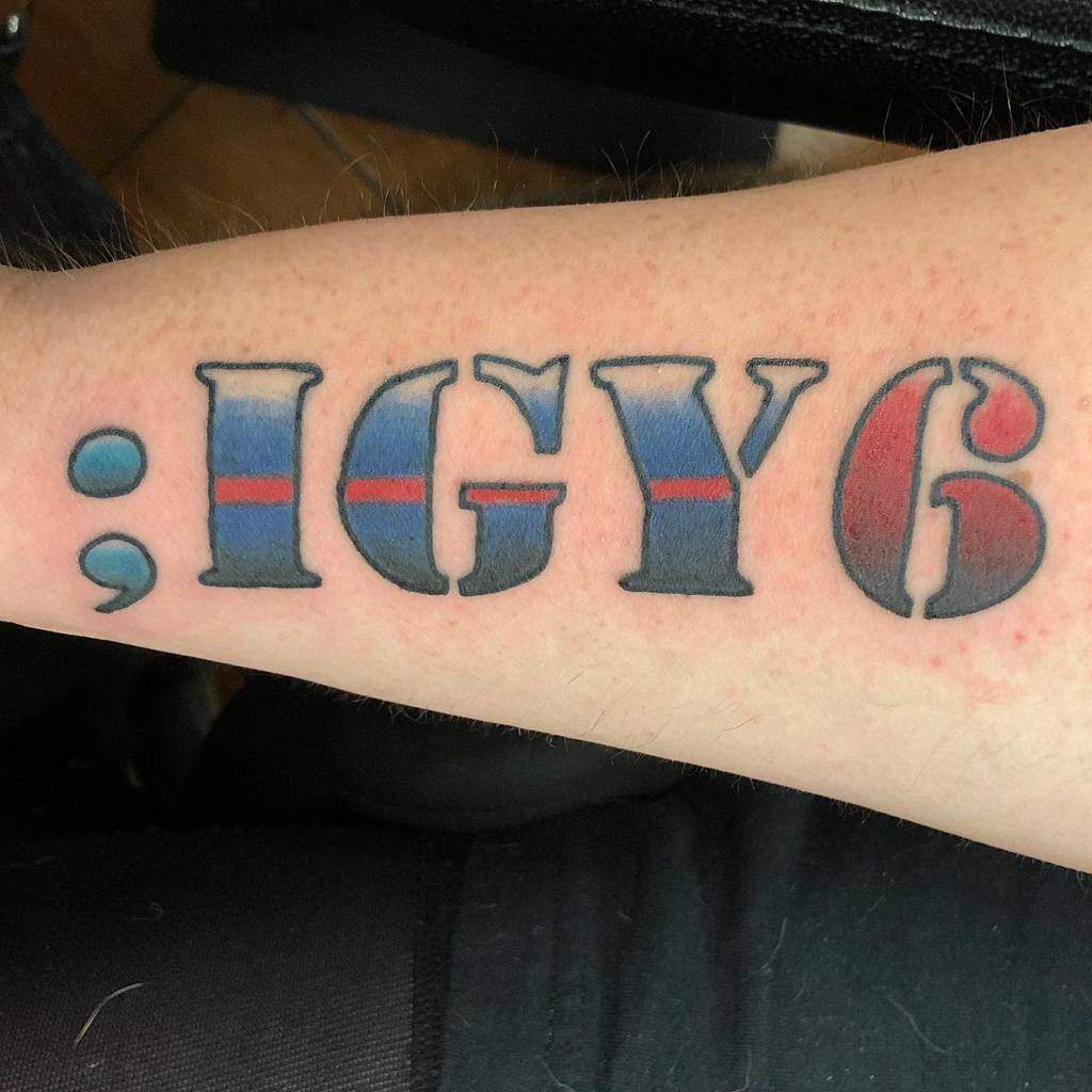 Forearm tattoo with the text ";IGY6" in bold, colored with blue and red stripes inside each character