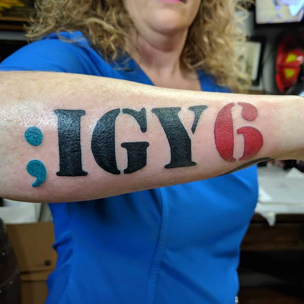 Woman showing a forearm tattoo with the text ";IGY6" in blue, black, and red