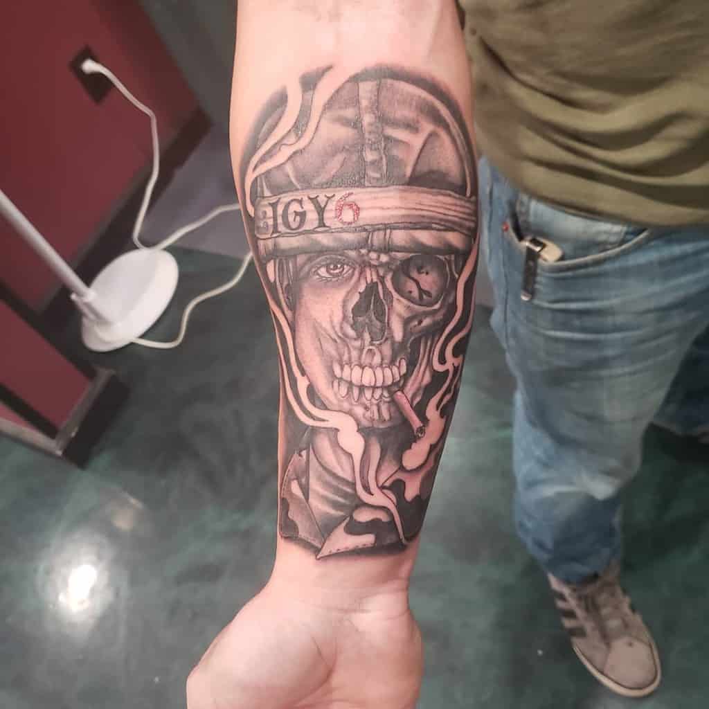 Forearm tattoo of a soldier's half-skull face with 'IGY6' on a headband, detailed shading, and a cigarette in the mouth