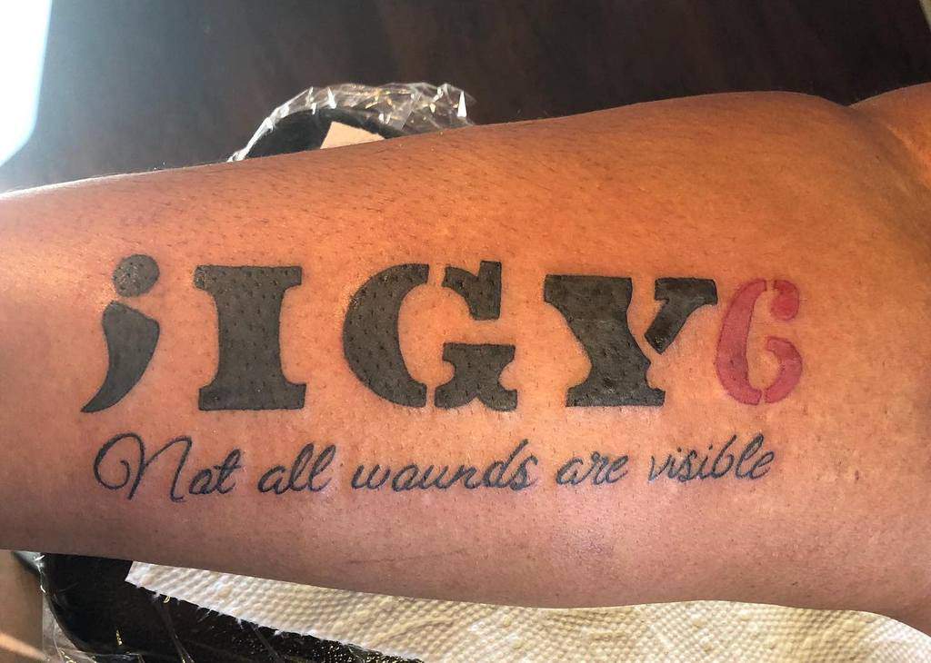 Tattoo on an arm reads ";IGY6" with a red "6" and "Not all wounds are visible" below