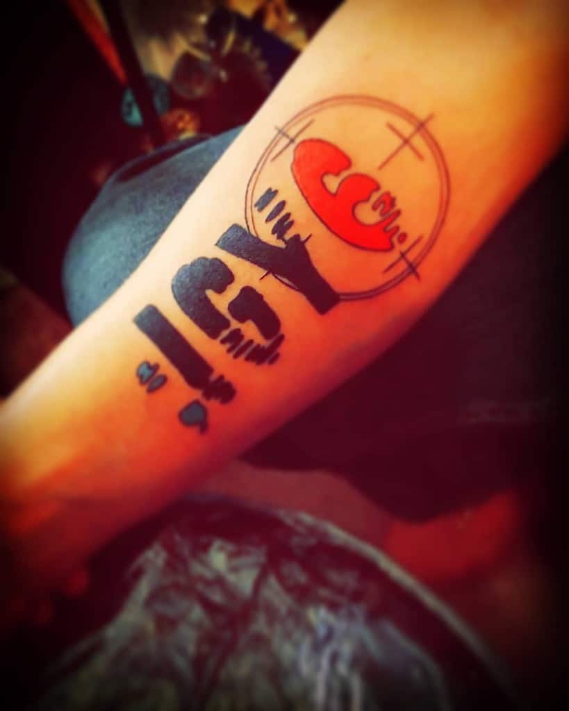 Forearm tattoo featuring ';IGY6' with a blue semicolon, red 6 inside a crosshair, and the number '22,' symbolizing veteran support