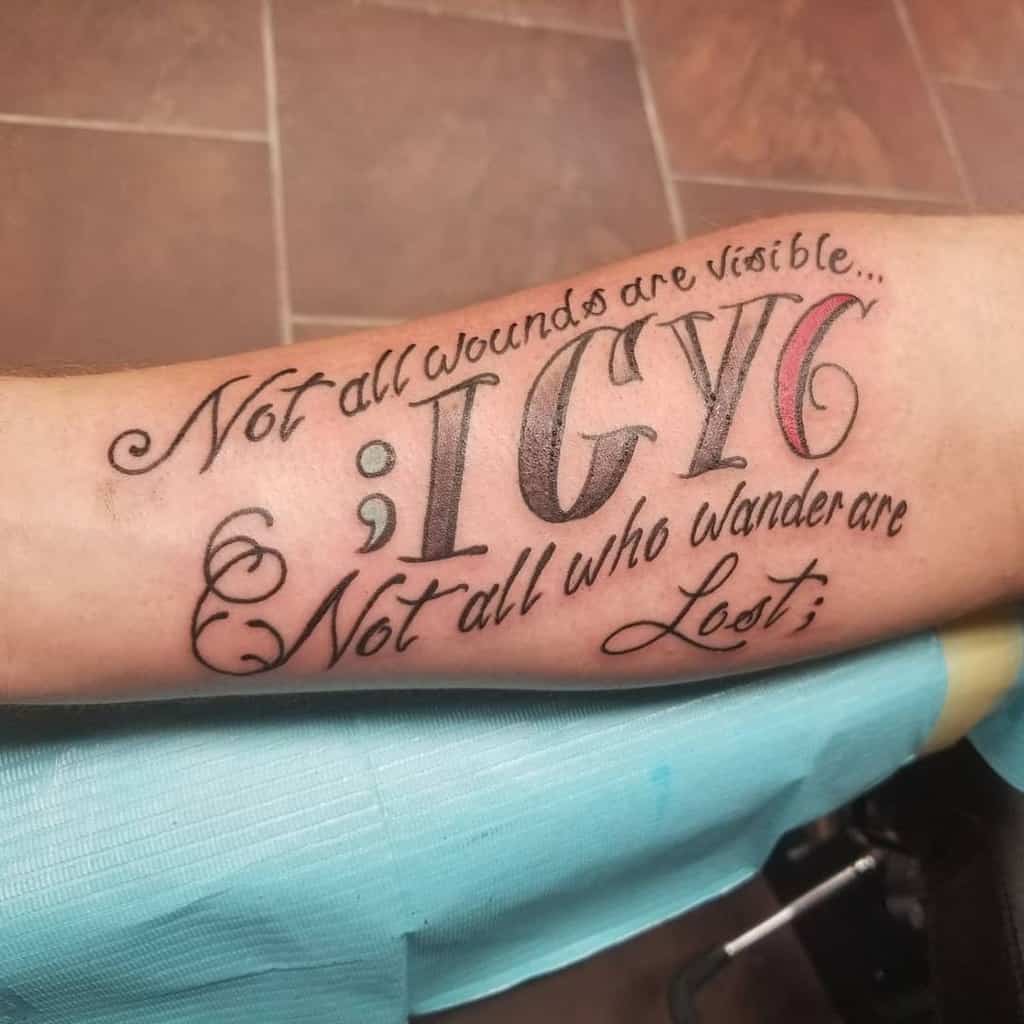 Forearm tattoo with ';IGY6,' a blue semicolon, red 6, and the phrases 'Not all wounds are visible...' and 'Not all who wander are lost'