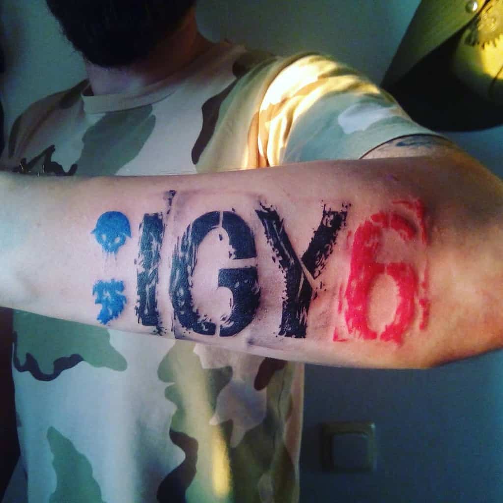 An arm tattoo with blue semicolon, black "IGY," and red "6"