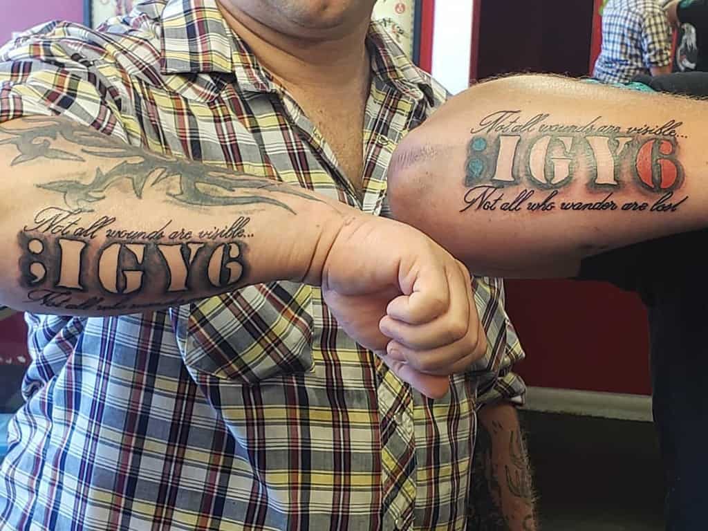 Two people showing forearm tattoos with the text: ";IGY6" and "Not all wounds are visible. Not all who wander are lost"