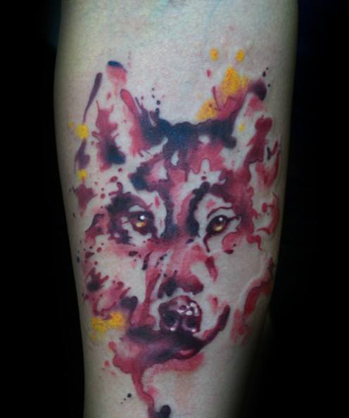 Watercolor wolf tattoo in fiery red and orange tones with fluid, abstract splashes and glowing eyes for a fierce, expressive design.
