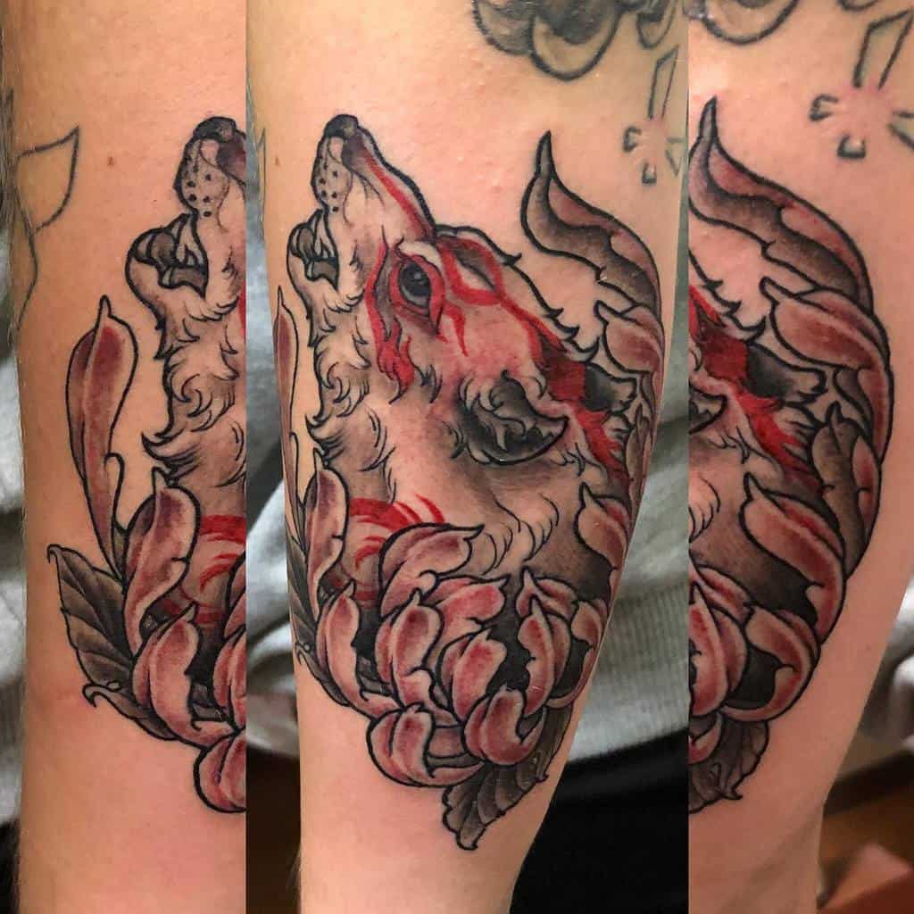 Japanese-style forearm tattoo featuring a howling wolf with bold red accents on its fur, surrounded by flowing, petal-like patterns and dark shading, creating a dynamic and traditional design