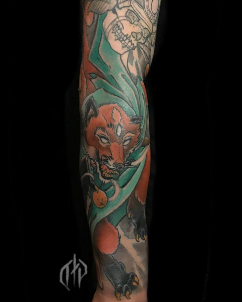 Forearm tattoo featuring a Japanese-style wolf with vibrant orange fur and teal accents, baring its teeth in a fierce stance