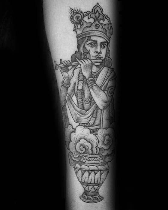 Black and grey Krishna tattoo showing him playing the flute, rising from a decorative pot with swirling clouds and intricate crown detail.