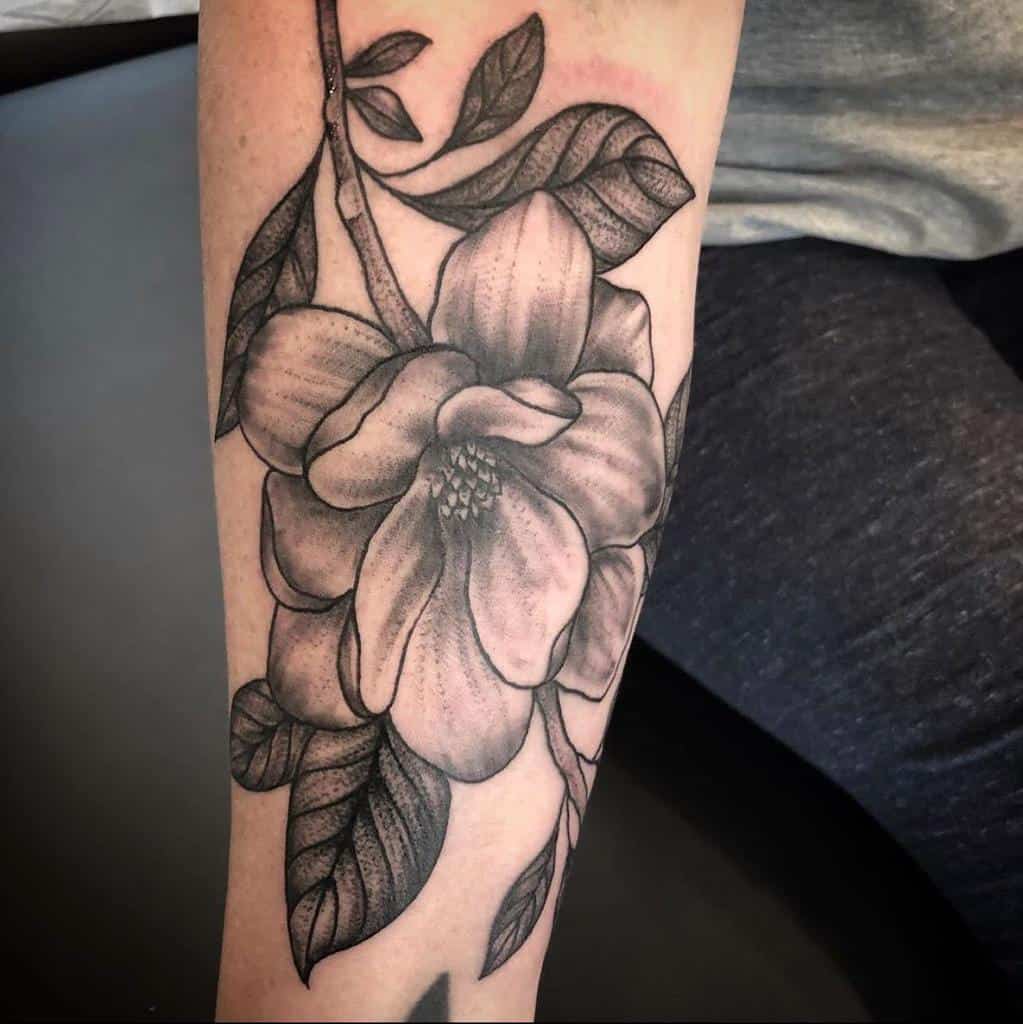 A stunning black and gray magnolia flower tattoo elegantly graces the forearm