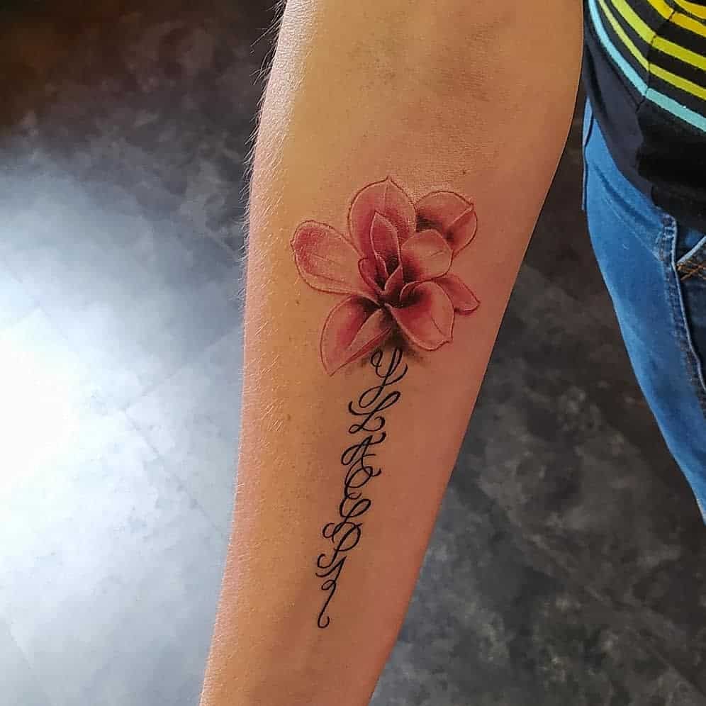 Forearm tattoo of a pink magnolia flower gracefully intertwined with ornamental script details