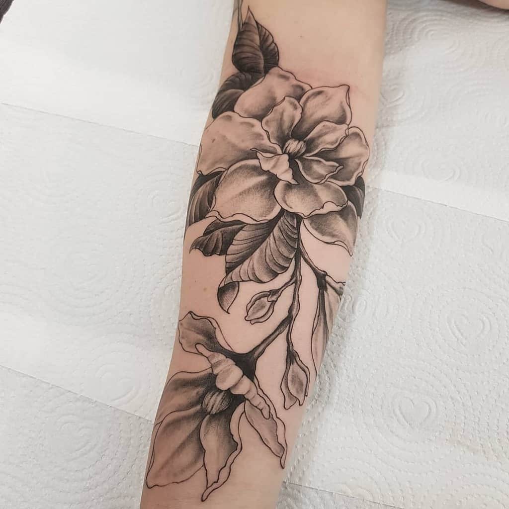 A stunning black and gray magnolia floral tattoo adorns the arm, showcasing detailed petals and leaves with exquisite craftsmanship