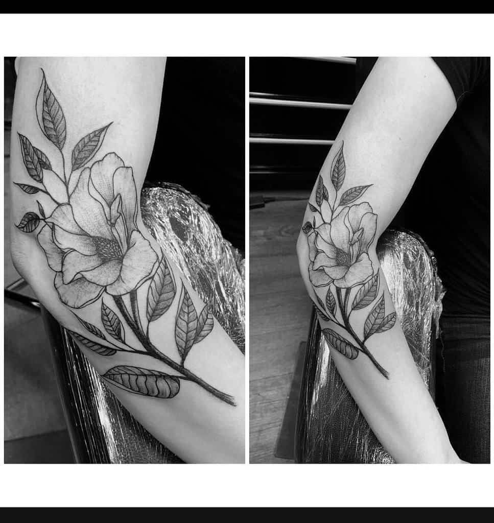 A black and white floral tattoo on a person's arm beautifully showcases detailed magnolia leaves and petals