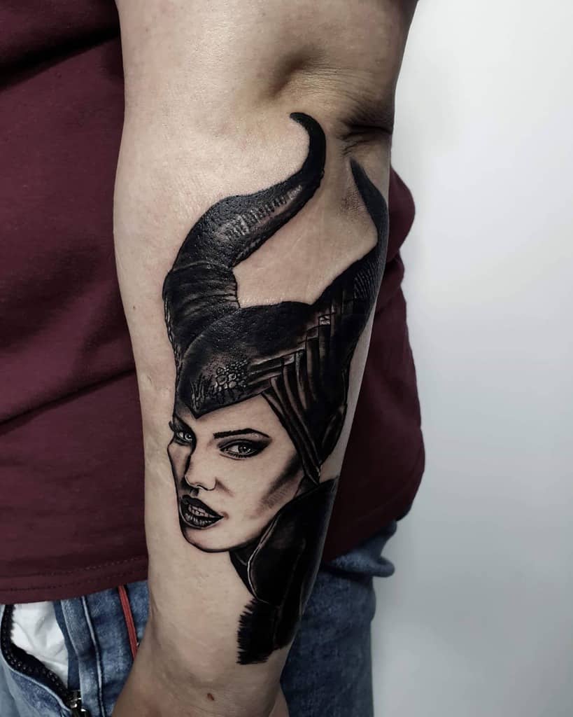 Detailed black-and-gray forearm tattoo of Maleficent with striking horns, bold features, and a commanding expression