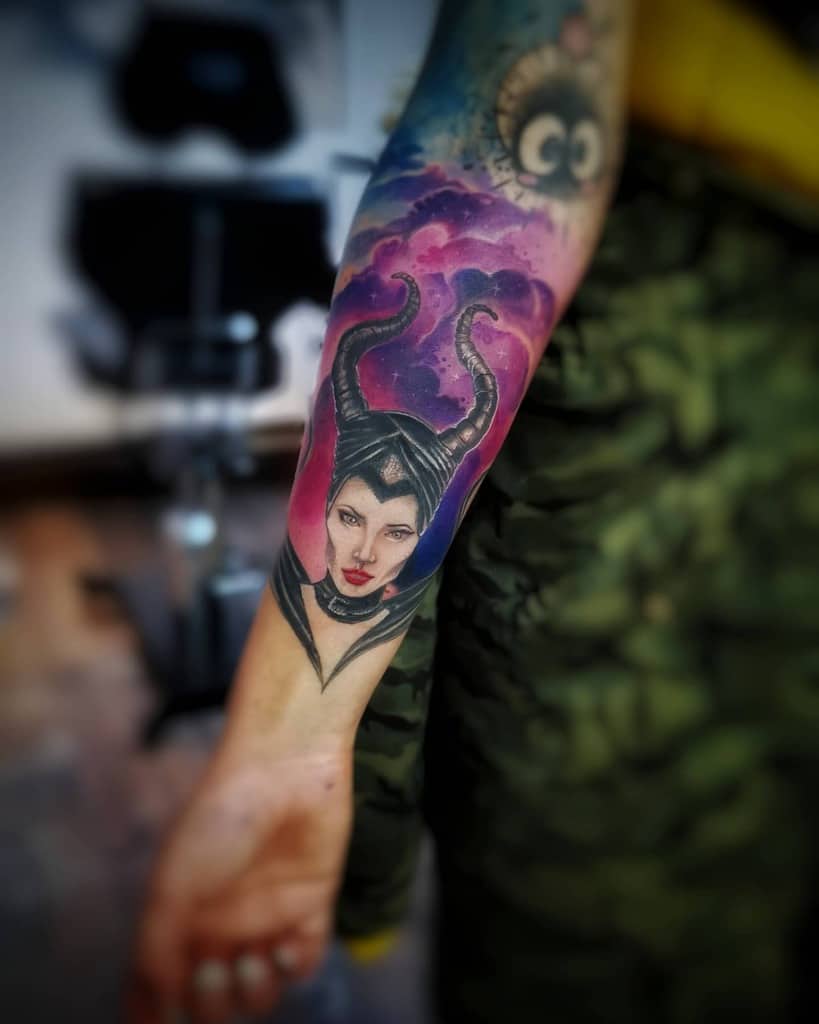 Colorful forearm tattoo of Maleficent, framed by vibrant purple and pink clouds, highlighting her iconic horns and piercing gaze