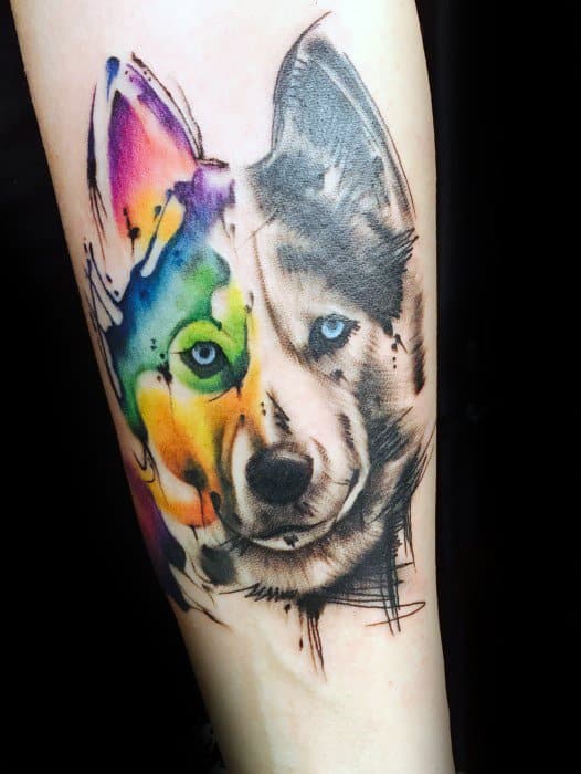 Half watercolor, half realistic wolf tattoo with vibrant rainbow colors on one side and detailed grayscale shading on the other.