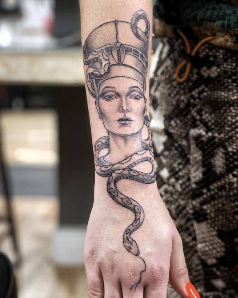 Striking tattoo portrays Queen Nefertiti adorned with a majestic cobra, symbolizing power and wisdom, with intricate detailing and shading on the forearm for a captivating design