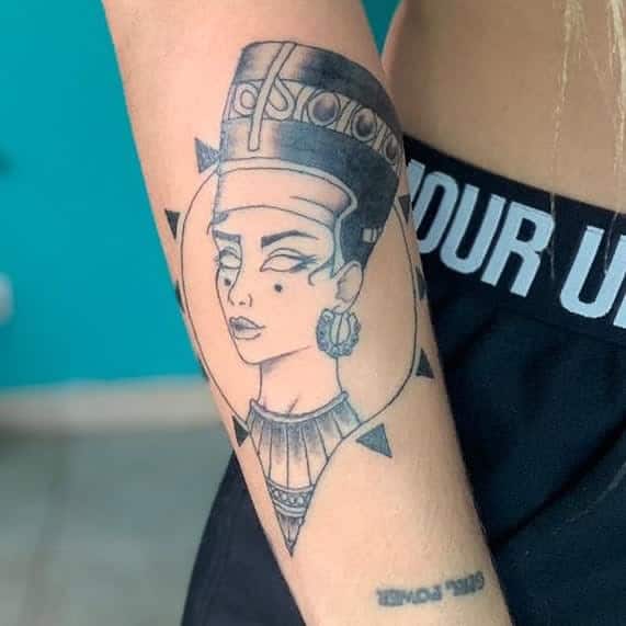 Forearm tattoo of Queen Nefertiti featuring a modern, illustrative style with bold black lines and subtle shading, framed within a circular design