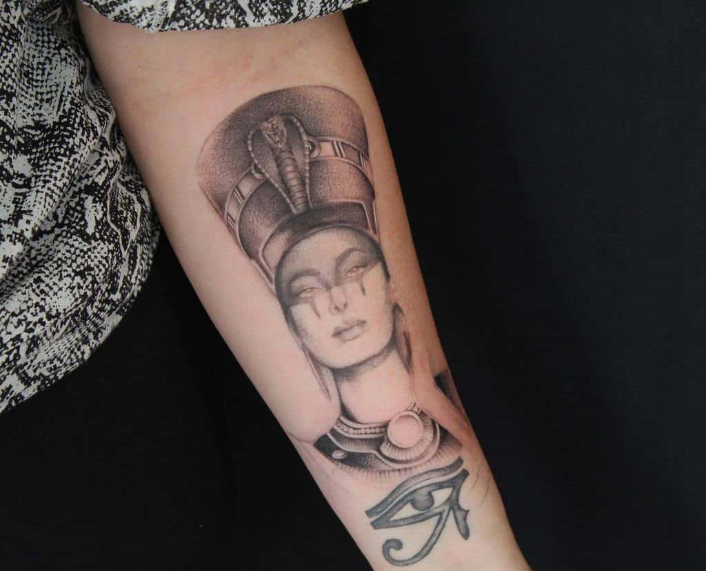 Black and grey tattoo of Nefertiti, an Egyptian queen, and Eye of Horus on a forearm