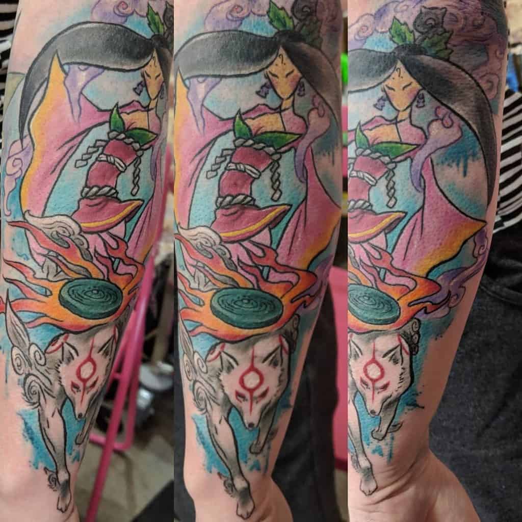 Vibrant Okami tattoo on the forearm featuring Amaterasu and a celestial goddess, blending fiery and pastel hues with flowing divine energy