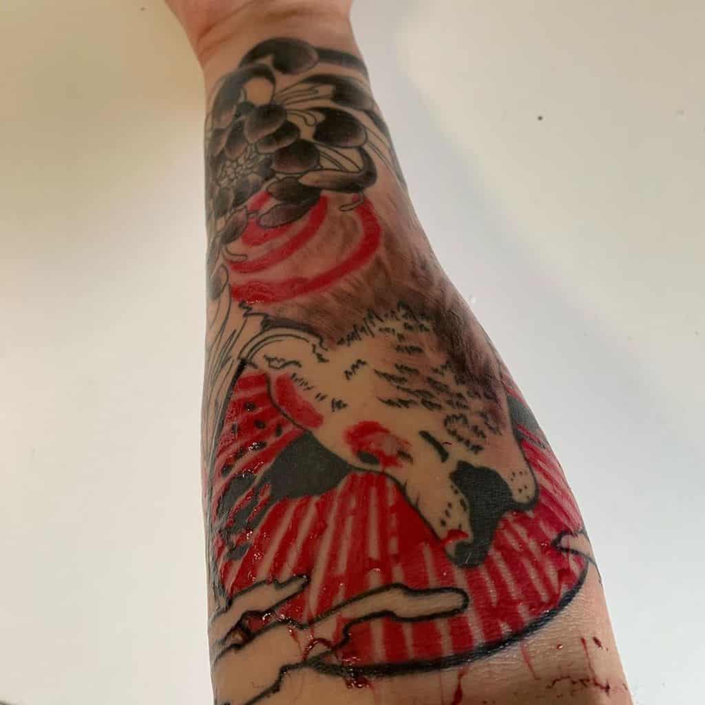 Bold Okami tattoo on the forearm featuring Amaterasu with striking red and black ink, incorporating a dynamic rising sun motif