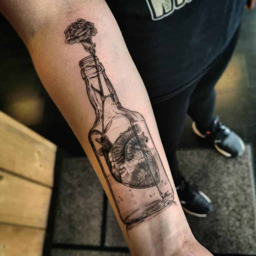 Forearm tattoo featuring a heart inside a glass bottle with a carnation growing from the top, done in fine linework for a surreal and symbolic design