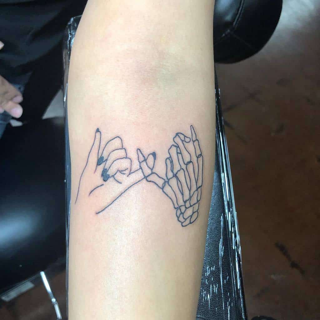Tattoo of two hands doing a pinky promise, one hand is skeletal and the other is normal, on a forearm