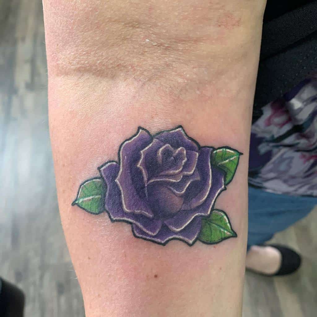 A stunning purple rose, brilliantly inked with lush green leaves, graces a person's arm