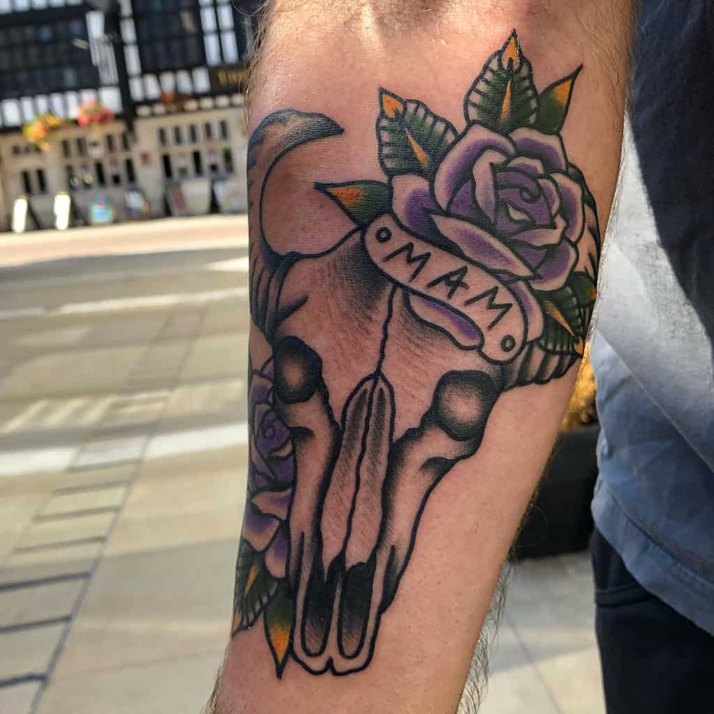 A captivating tattoo of a bull skull adorned with a vibrant purple rose graces the person's arm