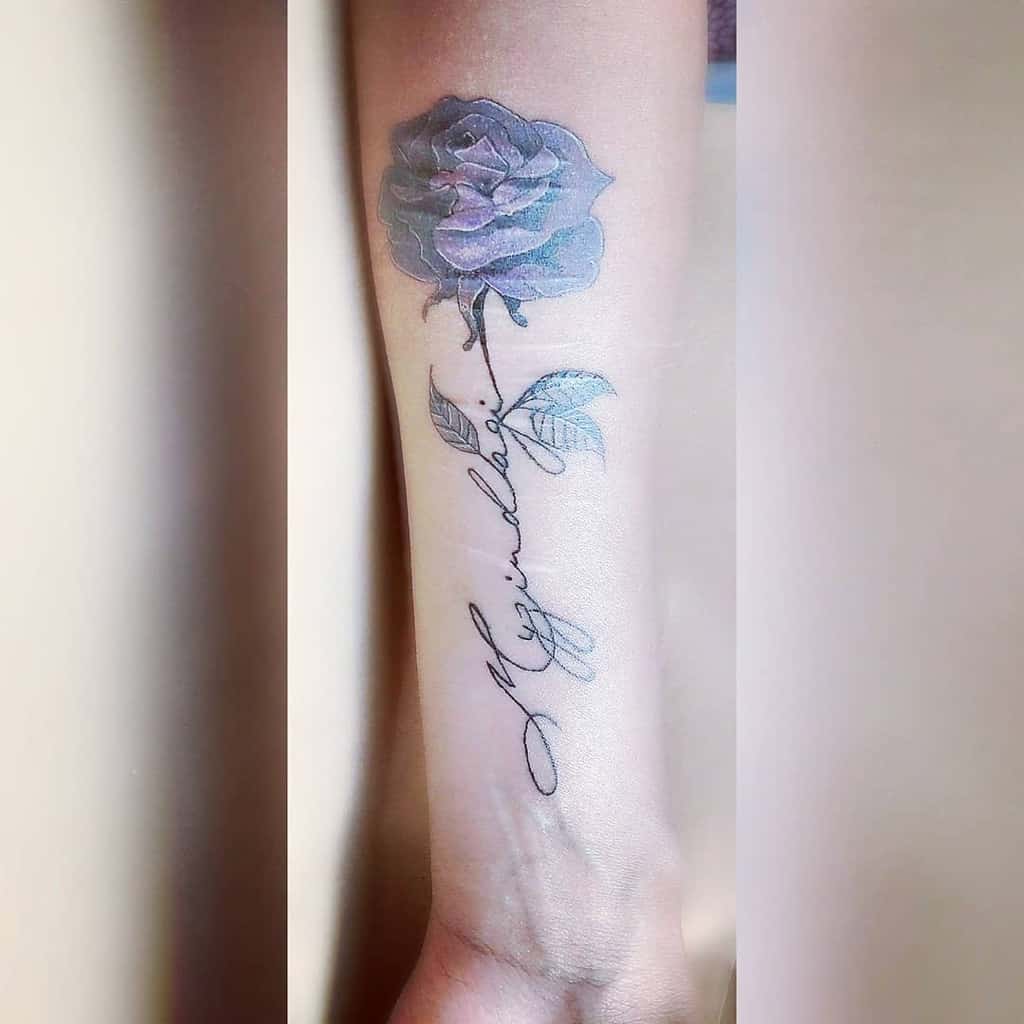 Tattoo on forearm featuring a striking blue rose intertwined with a purple rose, complemented by elegant cursive script below
