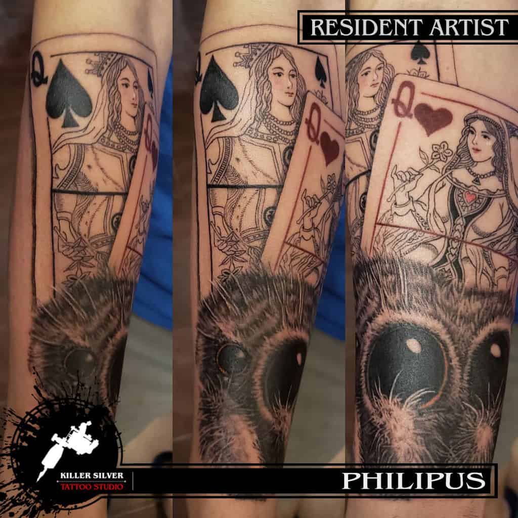 Forearm tattoo featuring intricate playing cards with the Queen of Spades and Queen of Hearts, highlighted by realistic shading