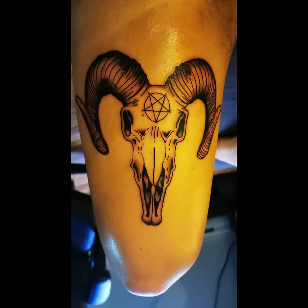 Tattoo of a ram's skull with a pentagram on the forehead, located on an arm
