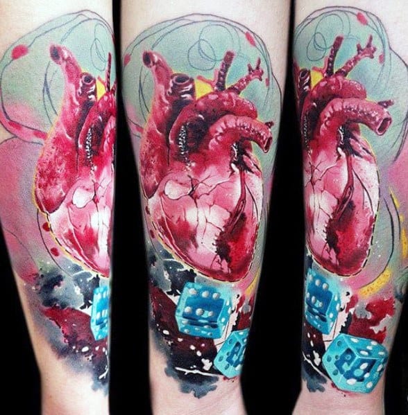 Tattoo of an anatomical heart intertwined with blue dice on an arm, featuring vibrant colors and abstract background elements