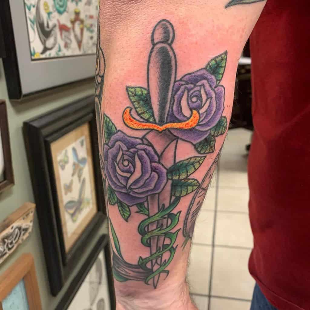 Forearm tattoo with a dagger, purple roses, and green leaves