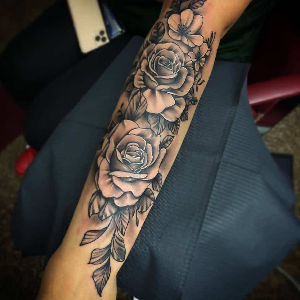 Forearm sleeve tattoo featuring large, detailed roses and leaves in black and gray tones