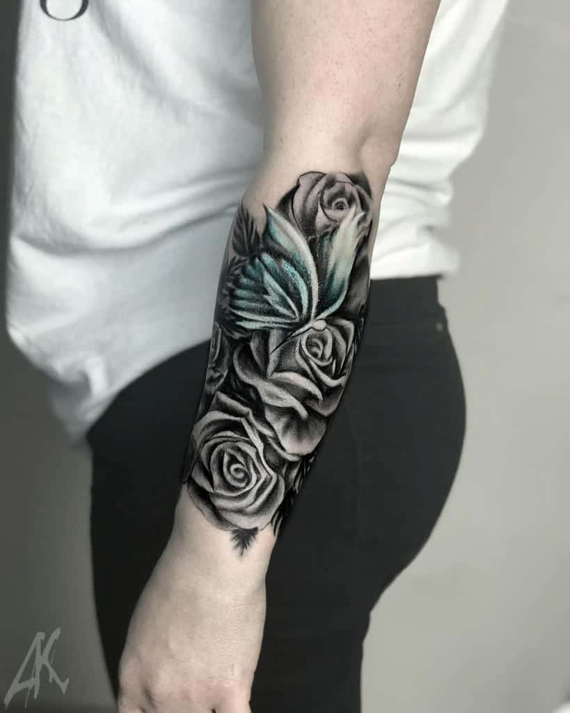 Forearm sleeve tattoo of intricate black roses entwined with a delicate teal butterfly