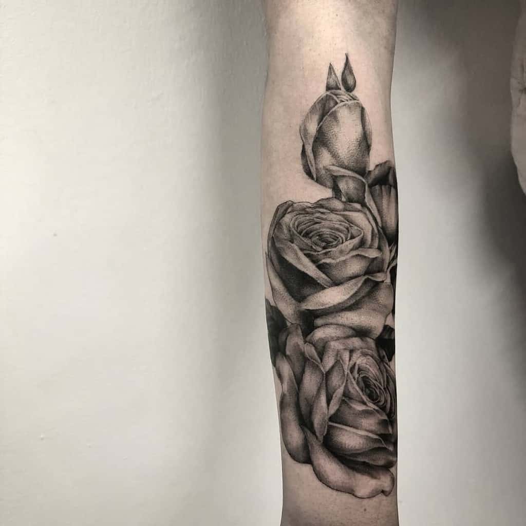 A stunning black and gray realistic rose tattoo gracefully adorns a forearm, seamlessly blending into a sleeve design