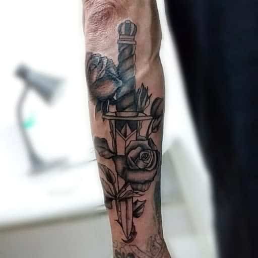 Forearm tattoo featuring a dagger piercing through a rose, with detailed shading and intertwining leaves creating a bold, symbolic design