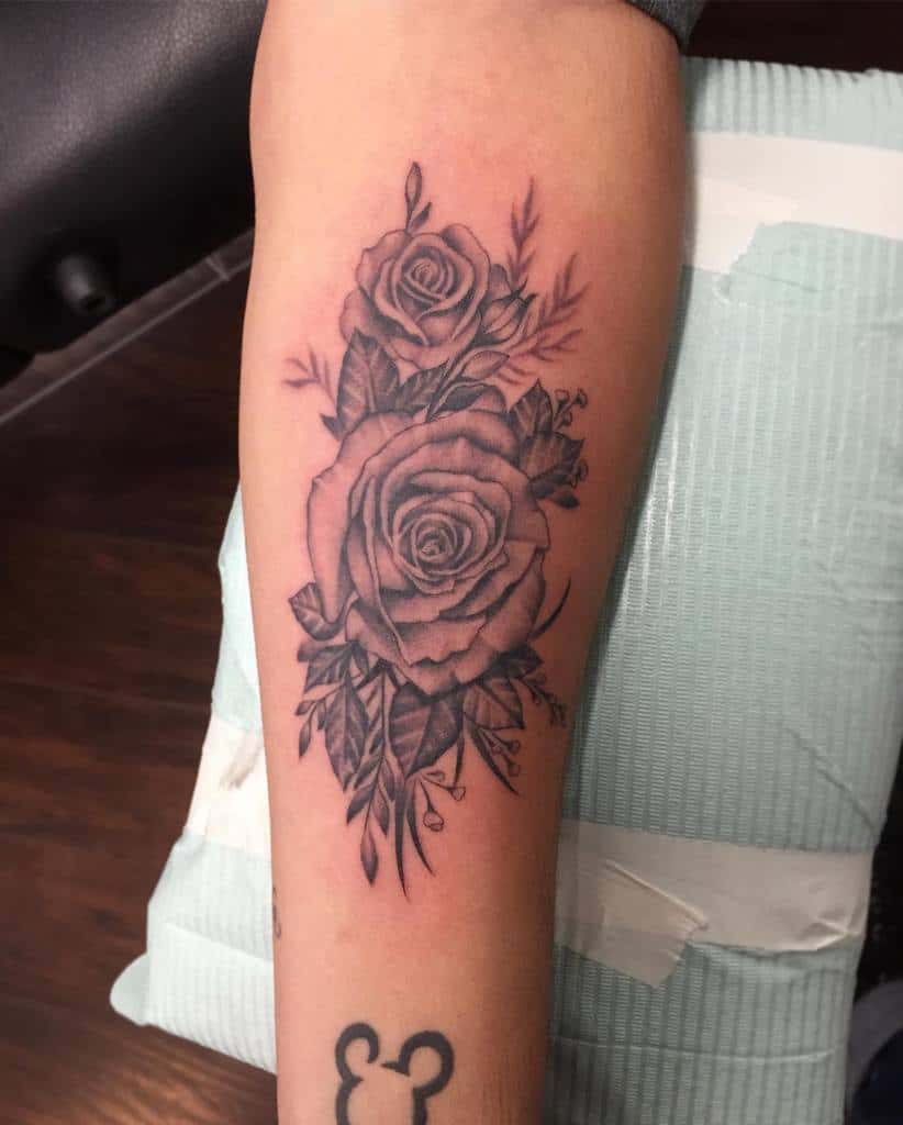 Forearm tattoo with two detailed roses and intricate leafy accents, shaded in black and grey for a timeless and elegant look.