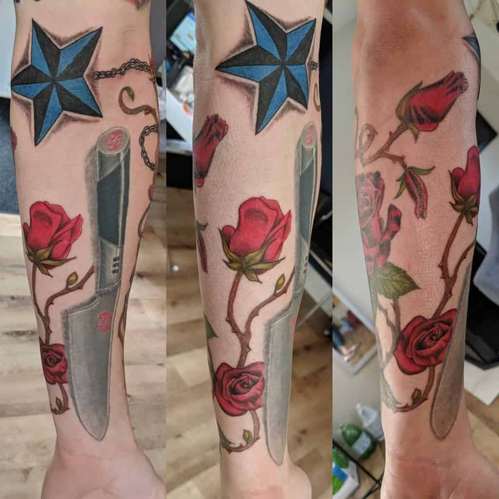 Forearm tattoo combining vibrant red roses with a dagger, blue star, and chain details, creating a bold and symbolic design